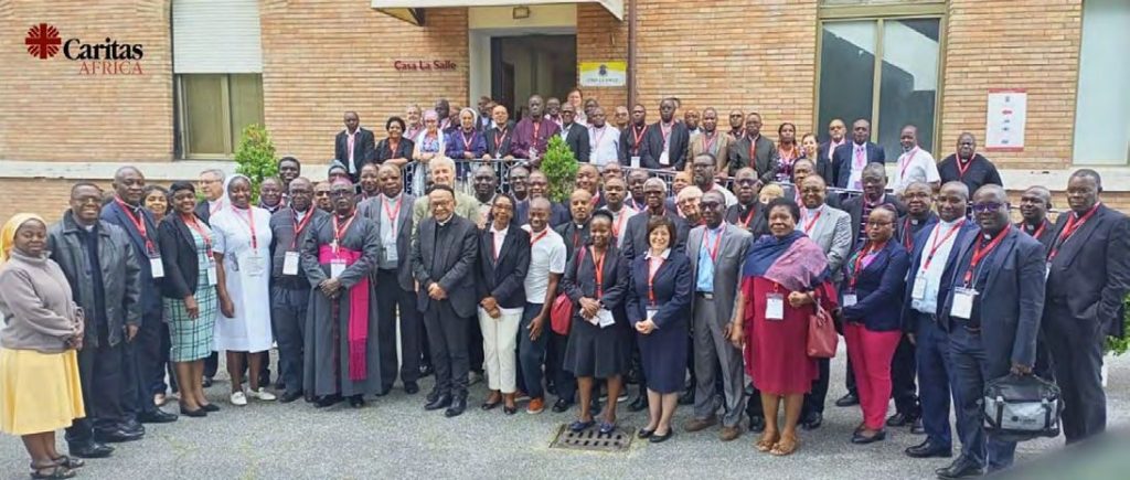 Plusieurs dizaines de membres du réseau, évêques, religieuses et laïcs, posent devant un bâtiment portant le logo de Caritas Africa.