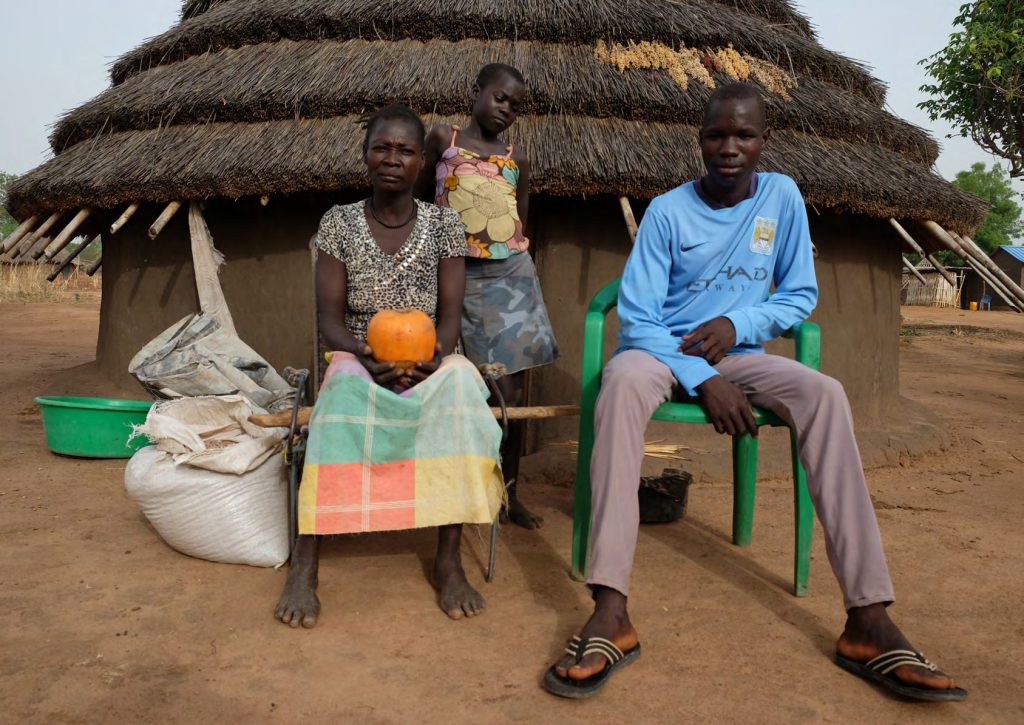 Une famille assise devant sa case au toit de chaume, près de sacs de vivres.