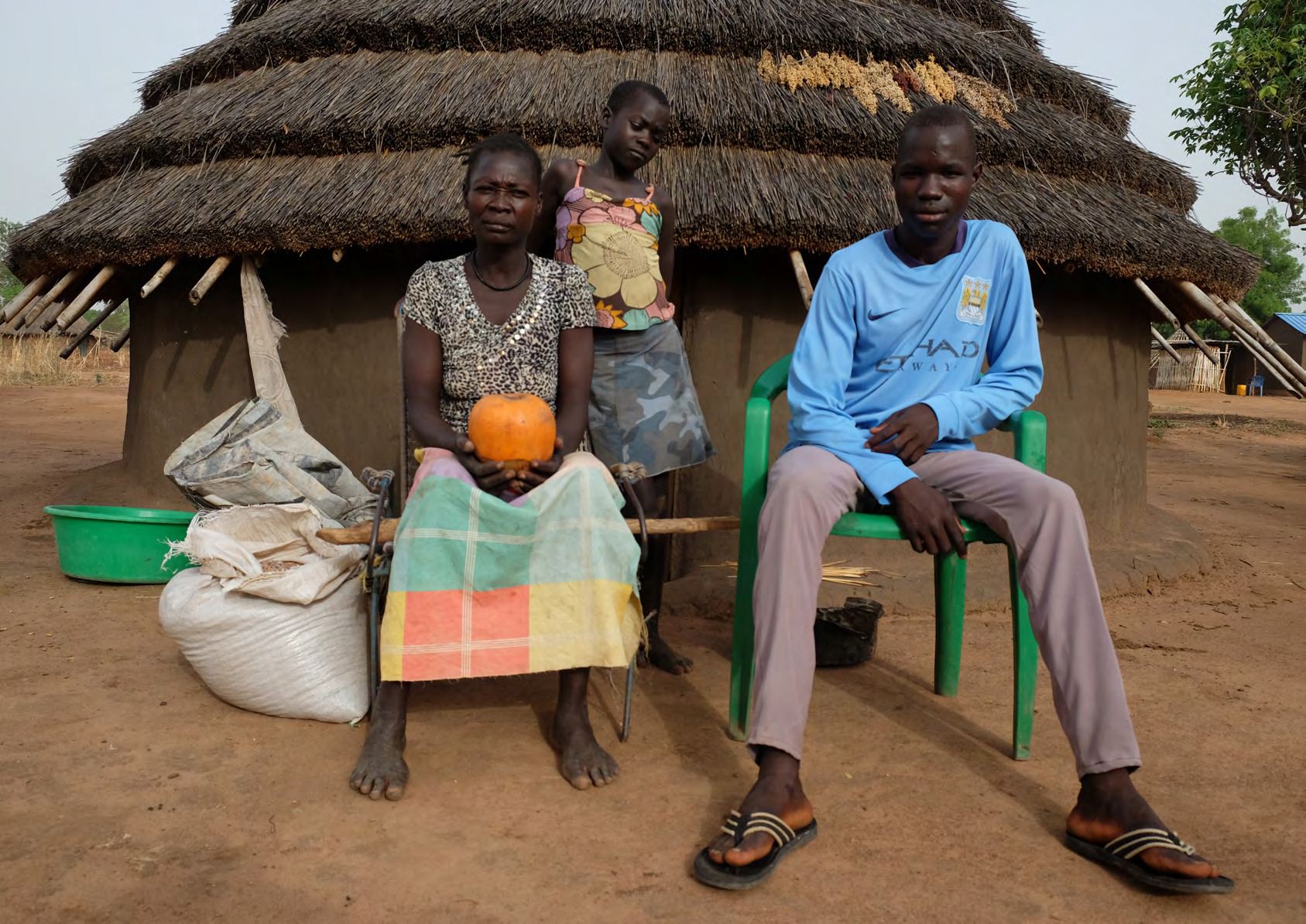 Une famille assise devant sa case au toit de chaume, près de sacs de vivres.