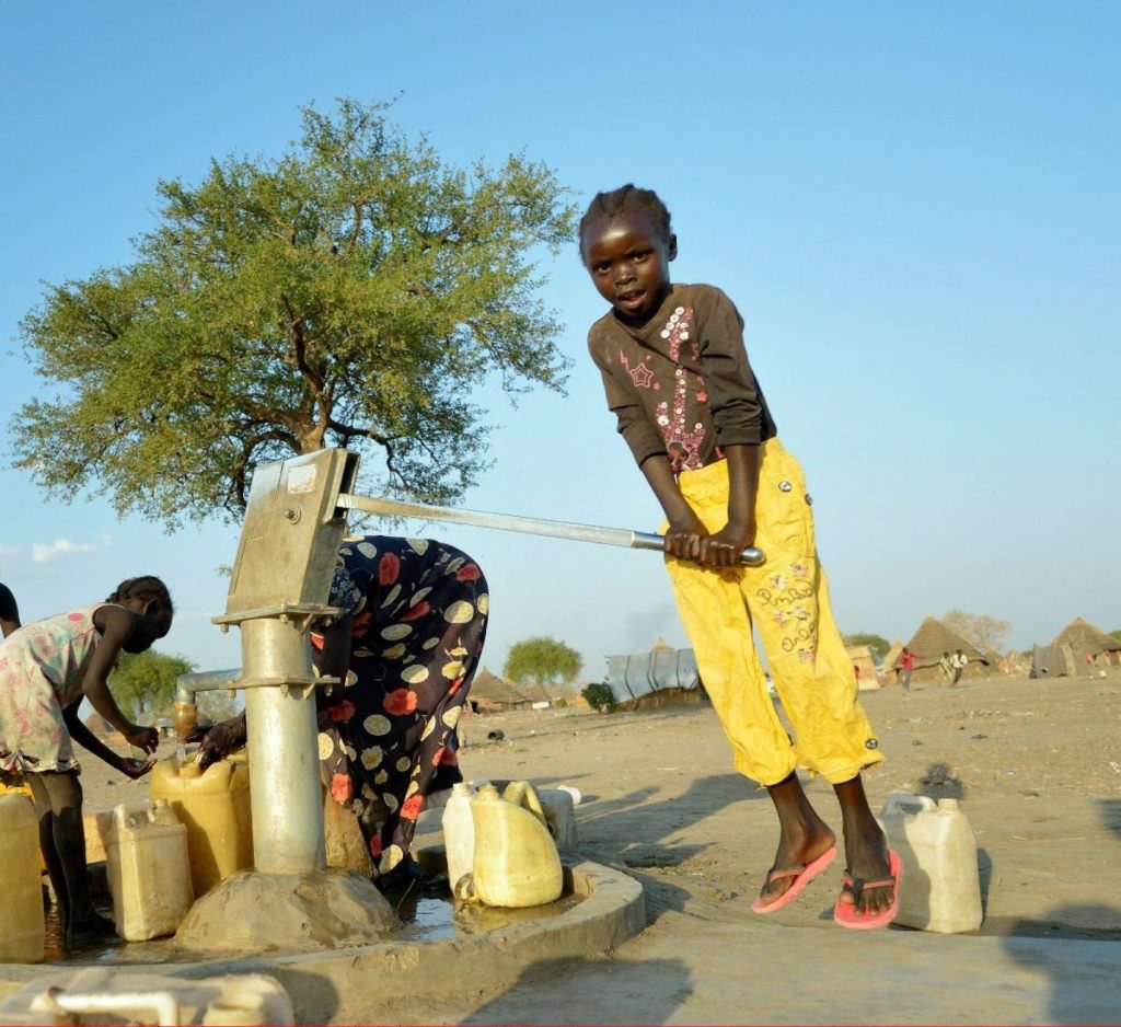 Une fillette actionne une pompe à eau manuelle pendant que d'autres enfants remplissent des bidons.