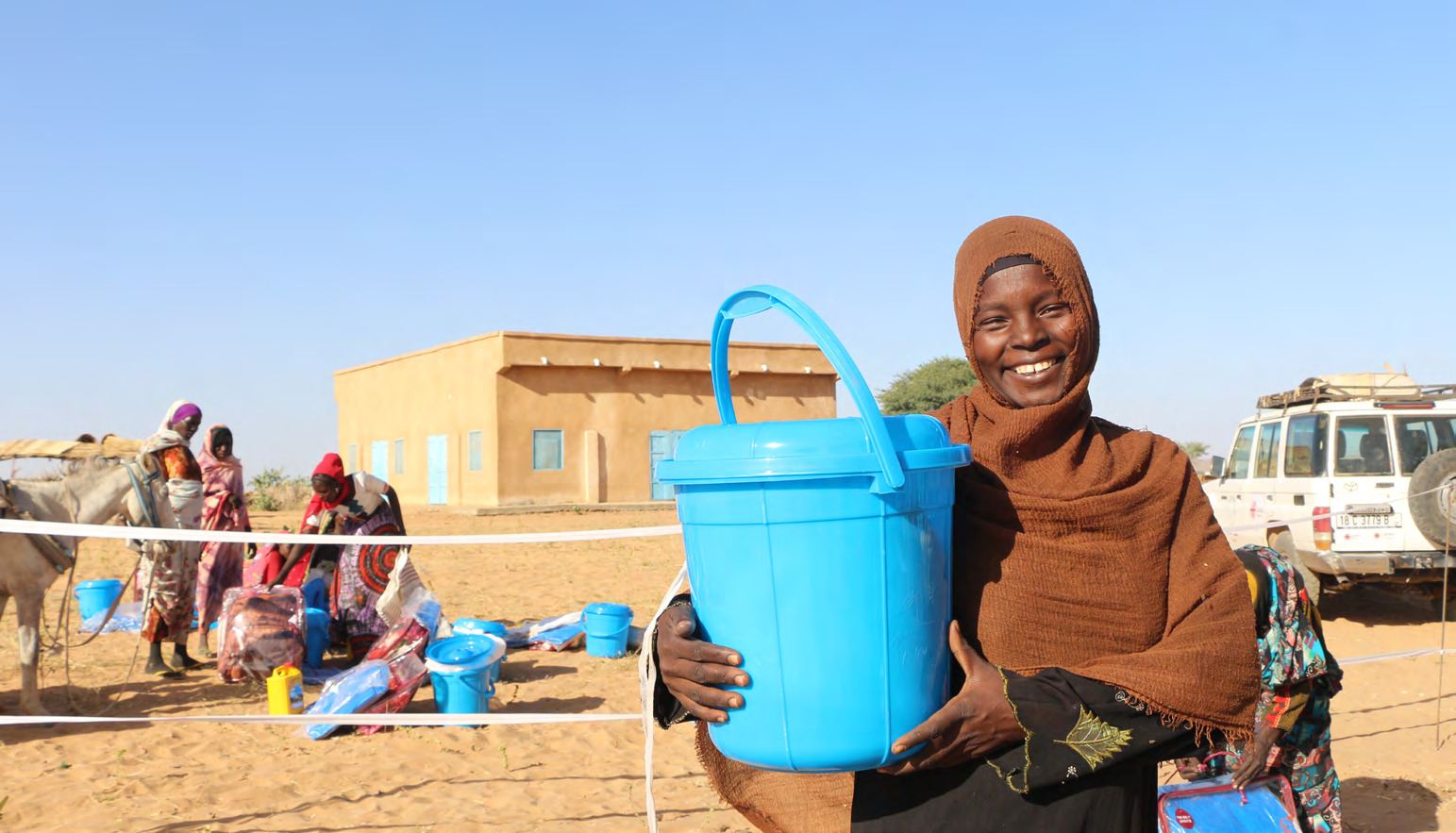 Une femme sourit en tenant le seau bleu qu'elle vient de recevoir lors d'une distribution.